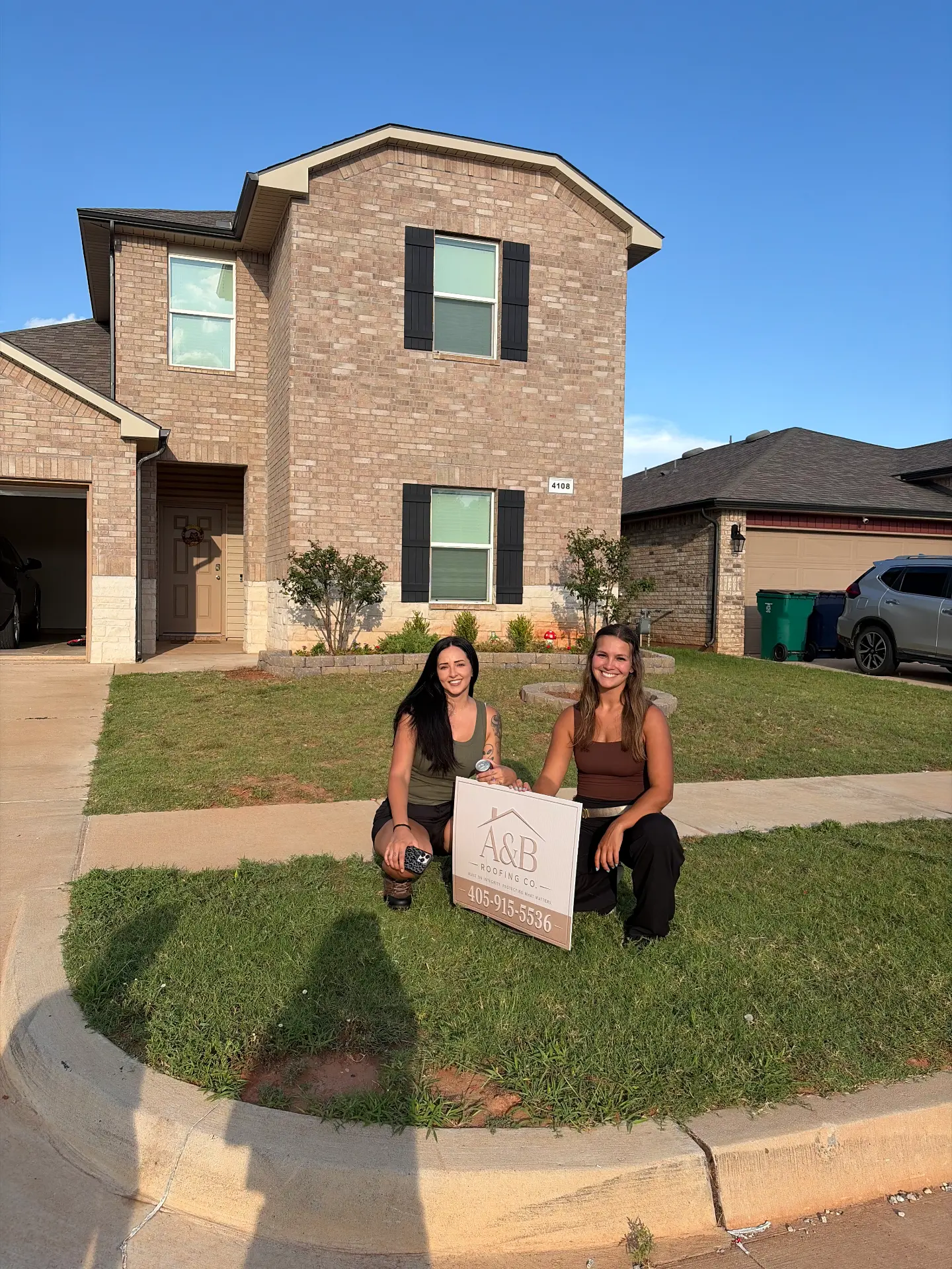 Two founders kneeling with a yard sign in front of a finished home