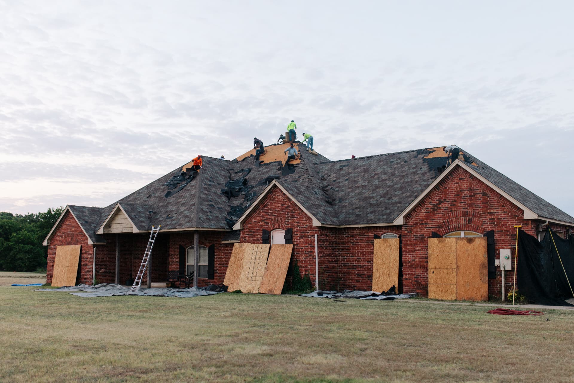 A brick home mid tear off with the crew across the roof