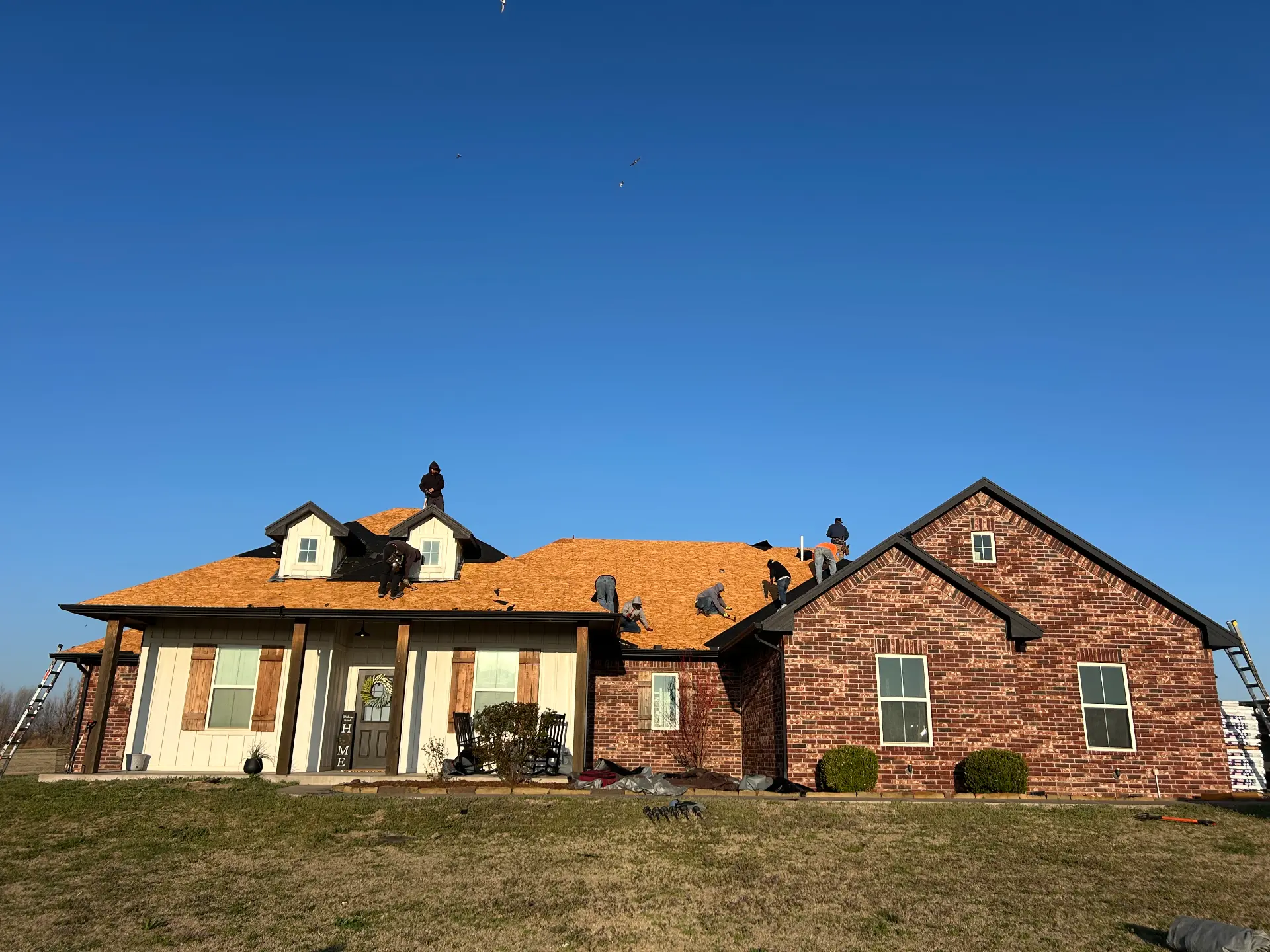 A crew decking a farmhouse roof under a clear winter sky