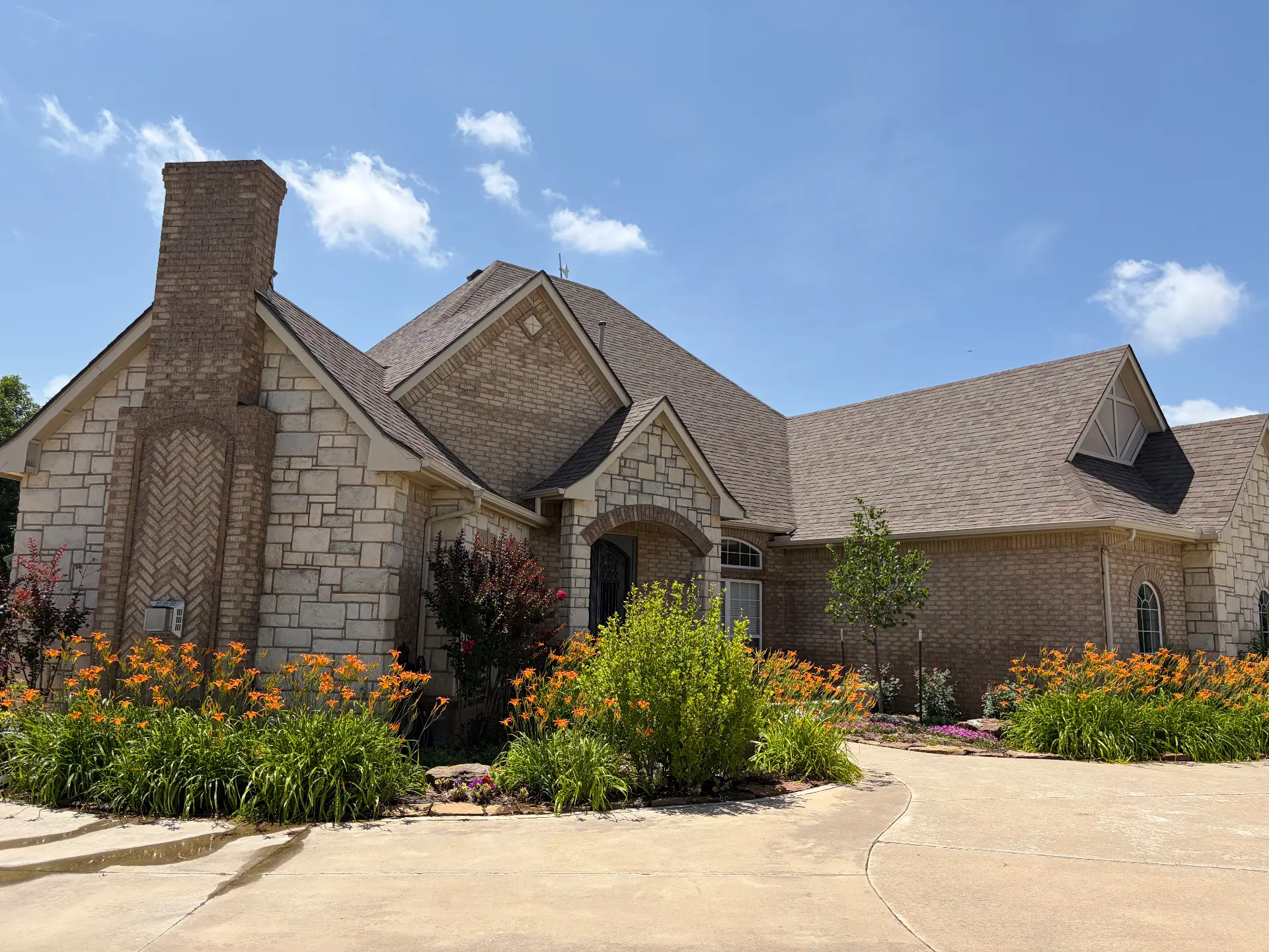 A stone and brick home with a finished roof in full summer bloom