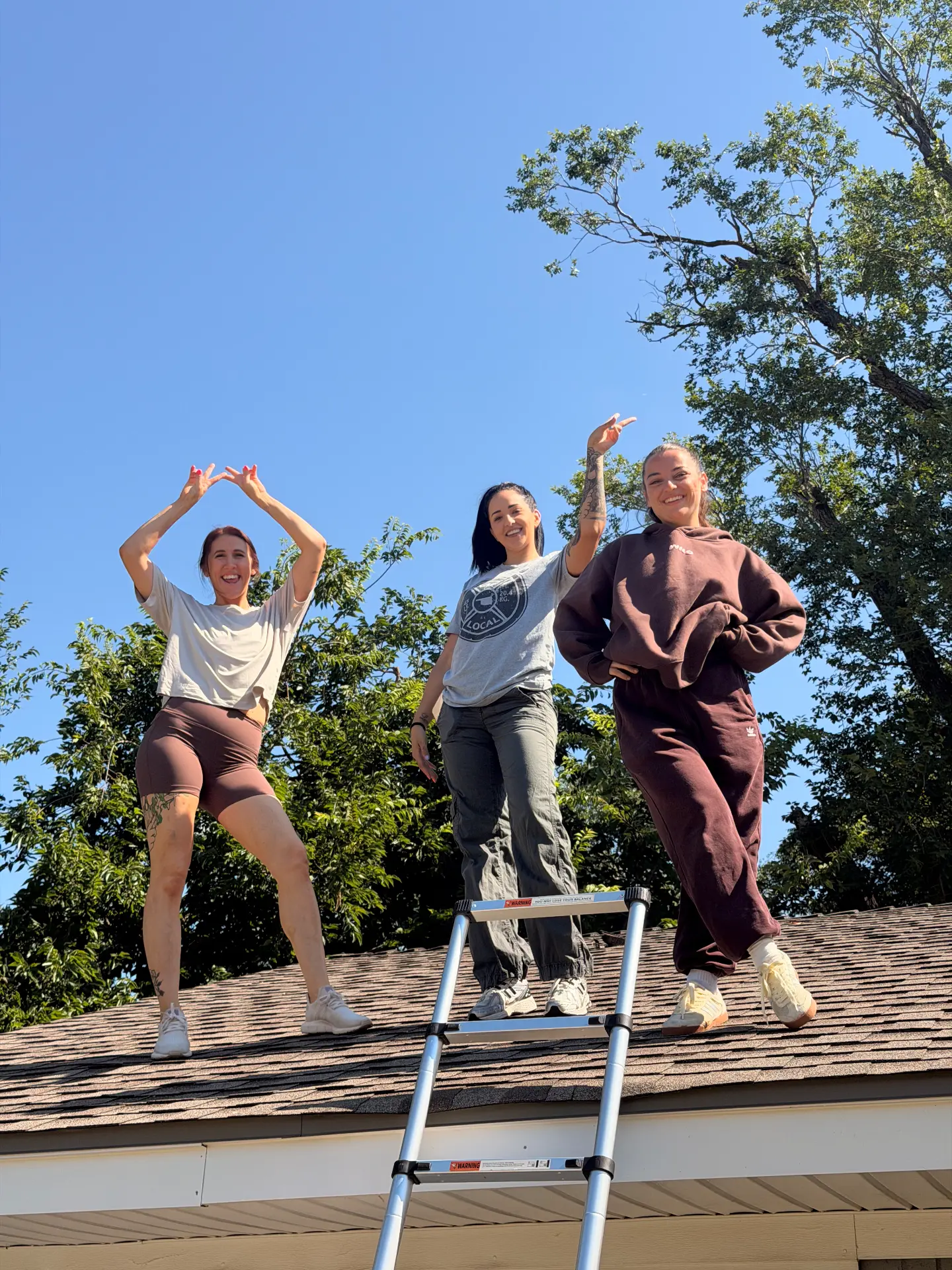 Three team members on a rooftop making a roof shape with their arms
